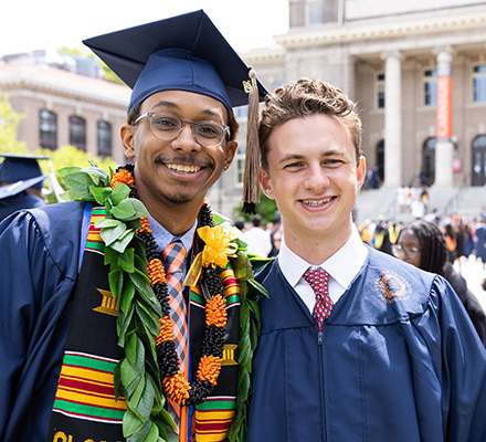 Two undergraduate degree recipients smile out front of Carnegie