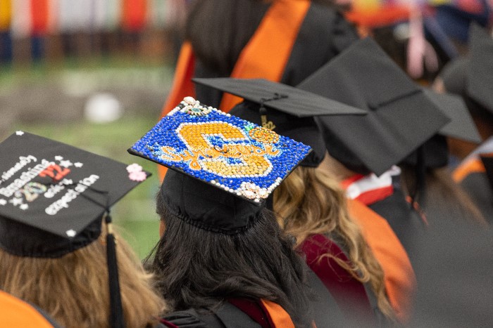 Focused shot of the top of a 2022 SU graduate’s cap featuring a bedazzled orange block S on a blue background