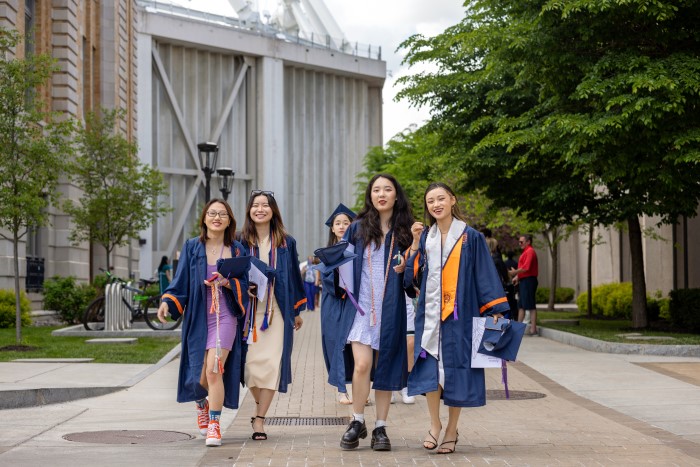 Group of five female graduates walking outside from JMA Wireless Dome to the Quad following the 2022 Commencement ceremony