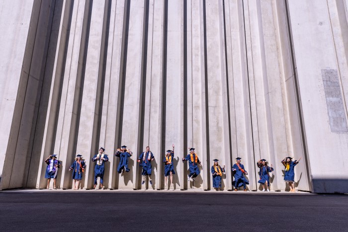 Group of graduates celebrate together by jumping between the pillars on the outside of the JMA Wireless Dome