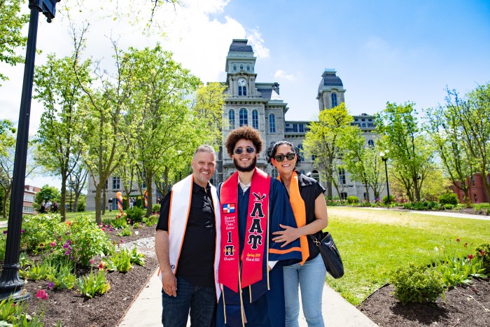 A Class of 2022 graduate poses with his parents on campus in front of the Hall of Languages